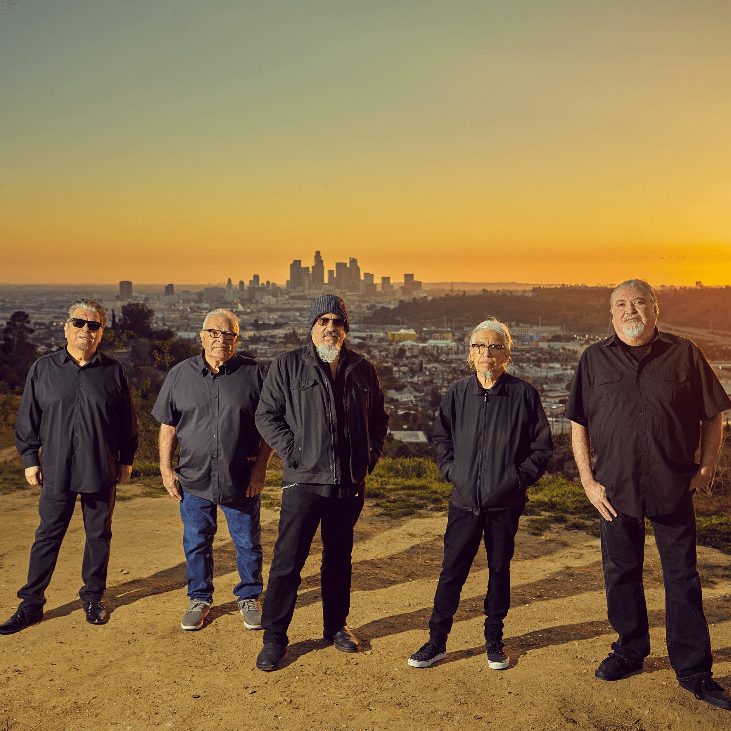 Image of Los Lobos standing on a hill at sunset with city skyline behind