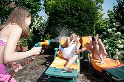 woman holding water hose and spraying her friends who are on banana lounges